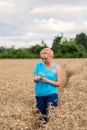 Beautiful woman stand in golden wheat field and hold ear of wheat, with cloudy blue sky background. Royalty Free Stock Photo