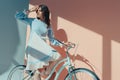 Beautiful woman standing in fashionable turquoise dress with long sleeves and sitting on bicycle and looking