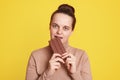 Beautiful woman standing isolated over yellow background and biting bar of chocolate, feels hungry, wearing casual beige sweater,