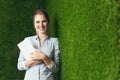 Beautiful woman standing over a green grass wall, holding a tablet Royalty Free Stock Photo