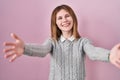 Beautiful woman standing over pink background looking at the camera smiling with open arms for hug Royalty Free Stock Photo