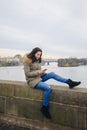 Beautiful woman standing by river in city Prague, text messaging. girl looking at phone on riverbank, with Prague bridge