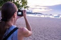 Beautiful woman standing taking a photo of sunset. Happy young woman with a camera and a backpack.