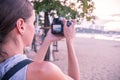 Beautiful woman standing taking a photo of sunset. Happy young woman with a camera and a backpack.