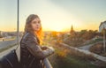 A beautiful woman stands on the bridge and looks at the sunset, looking thoughtfully. The girl is in a thoughtful mood