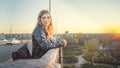 A beautiful woman stands on the bridge and looks at the sunset, looking thoughtfully. The girl is in a thoughtful mood