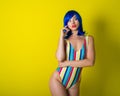 Beautiful woman in a striped swimsuit in a blue wig posing on a yellow background. Portrait of a glamorous girl. Royalty Free Stock Photo