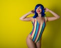 Beautiful woman in a striped swimsuit in a blue wig posing on a yellow background. Portrait of a glamorous girl. Royalty Free Stock Photo