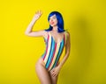 Beautiful woman in a striped swimsuit in a blue wig posing on a yellow background. Portrait of a glamorous girl. Royalty Free Stock Photo