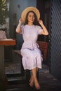 Beautiful young woman in stylish violet dress and straw hat sitting on bench outdoors Royalty Free Stock Photo