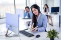 Beautiful woman in suit and headset opening book to check notes while talking to a costumer at call center. Royalty Free Stock Photo