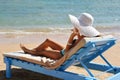 Beautiful woman sunbathing on a beach at tropical travel resort, enjoying summer holidays. Girl holding a hat with her Royalty Free Stock Photo