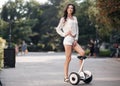 Beautiful long-haired brunette in a green park outdoors riding a scooter Royalty Free Stock Photo