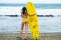 Beautiful woman surfer, sexy slim brunette in swimsuit with sporty buttocks holding yellow surfboard on sandy beach Royalty Free Stock Photo