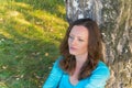 Beautiful woman in sweater resting next to the tree and thinkin