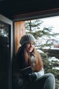 Beautiful woman in a sweater  sitting home by the window. Blurred winter snow tree background. Morning, coziness, winter and peopl Royalty Free Stock Photo