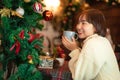 Beautiful woman in sweater is smiling and holding cup to drinking hot coffee for relax in front of christmas tree Royalty Free Stock Photo