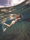 Beautiful woman is swimming diving among coral reefs in shallow water and looking underwater sealife, side view. Royalty Free Stock Photo