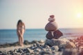 Beautiful woman in a swimsuit walking along the beach against the background of a pyramid of stones. Blurred female with stones on Royalty Free Stock Photo