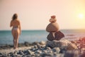 Beautiful woman in a swimsuit walking along the beach against the background of a pyramid of stones. Blurred female with stones on Royalty Free Stock Photo