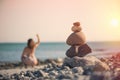 Beautiful woman in a swimsuit walking along the beach against the background of a pyramid of stones. Blurred female with stones on Royalty Free Stock Photo