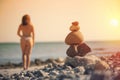 Beautiful woman in a swimsuit walking along the beach against the background of a pyramid of stones. Blurred female with stones on Royalty Free Stock Photo