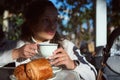 Beautiful woman takes her breakfast in the street cafe, drinks freshly brewed espresso coffee and eats crispy croissants Royalty Free Stock Photo