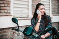 Beautiful woman talking at cell phone, while sitting on her scooter on the city street Royalty Free Stock Photo