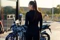 Back view of beautiful young woman in tight fitting black suit near sport motorcycle at self service car wash. Royalty Free Stock Photo