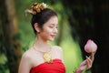 Beautiful woman in traditional Thai red dress and holding lotus flower in her hand in the nature black background Royalty Free Stock Photo