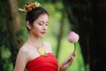 Beautiful woman in traditional Thai red dress and holding lotus flower in her hand in the nature black background Royalty Free Stock Photo