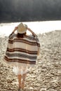 Beautiful woman traveler wearing hat and poncho walking at river beach, american outfit, boho concept, space for text Royalty Free Stock Photo