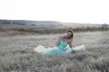 Beautiful woman in turquoise couture dress posing in frost covered field at sunrise