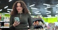 Beautiful woman use smartphone in supermarket. Woman buyer using mobile phone application standing with shopping trolley Royalty Free Stock Photo