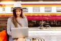 Beautiful woman is using laptop at train station before charming beautiful asian woman travel to destination. She is a blogger and