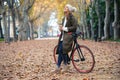 Beautiful woman with a vintage bike drinking coffee while cycling through the park in autumn Royalty Free Stock Photo