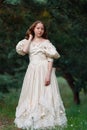 Beautiful woman in vintage dress beige. Cute girl in long dress walking in a pine forest. The style of the Queen