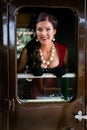 Beautiful female in vintage red dress looking at camera through train door window