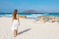 Beautiful woman walking on Corralejo beach looking at Lobos Island with stones shelters on the sand to protect from strong winds