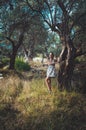 Beautiful woman walking in summer park with olive trees on sunset. Tanned brunette female long hair in white dress Royalty Free Stock Photo