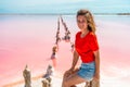 A beautiful woman walks on a salty beach between wooden sticks on a salty pink lake with a blue sky. A peaceful landscape and rela Royalty Free Stock Photo