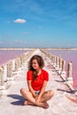 A beautiful woman walks on a salty beach between wooden sticks on a salty pink lake with a blue sky. A peaceful landscape and rela Royalty Free Stock Photo