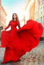 Beautiful Woman in Waving Long Fluttering Red Dress Walking on the City Street. Outdoor Brunette Portrait in Sun Royalty Free Stock Photo