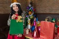 Beautiful woman wear red dress and santa claus hat showing green gift bag on hand in restaurant. Royalty Free Stock Photo