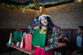 Beautiful woman wear red dress and santa claus hat showing green gift bag on hand in restaurant. concept of Christmas party Royalty Free Stock Photo