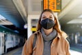 Beautiful woman wearing black face mask FFP2 KN95 in train station with timetables on background Royalty Free Stock Photo