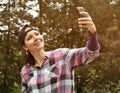 Beautiful woman wearing checked shirt and baseball cap taking selfie in the city park.