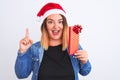 Beautiful woman wearing Christmas Santa hat holding gift over isolated white background surprised with an idea or question Royalty Free Stock Photo