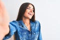 Beautiful woman wearing denim shirt make selfie by camera over isolated white background looking away to side with smile on face, Royalty Free Stock Photo