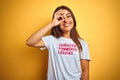 Beautiful woman wearing fanny t-shirt with irony comments over isolated yellow background doing ok gesture with hand smiling, eye